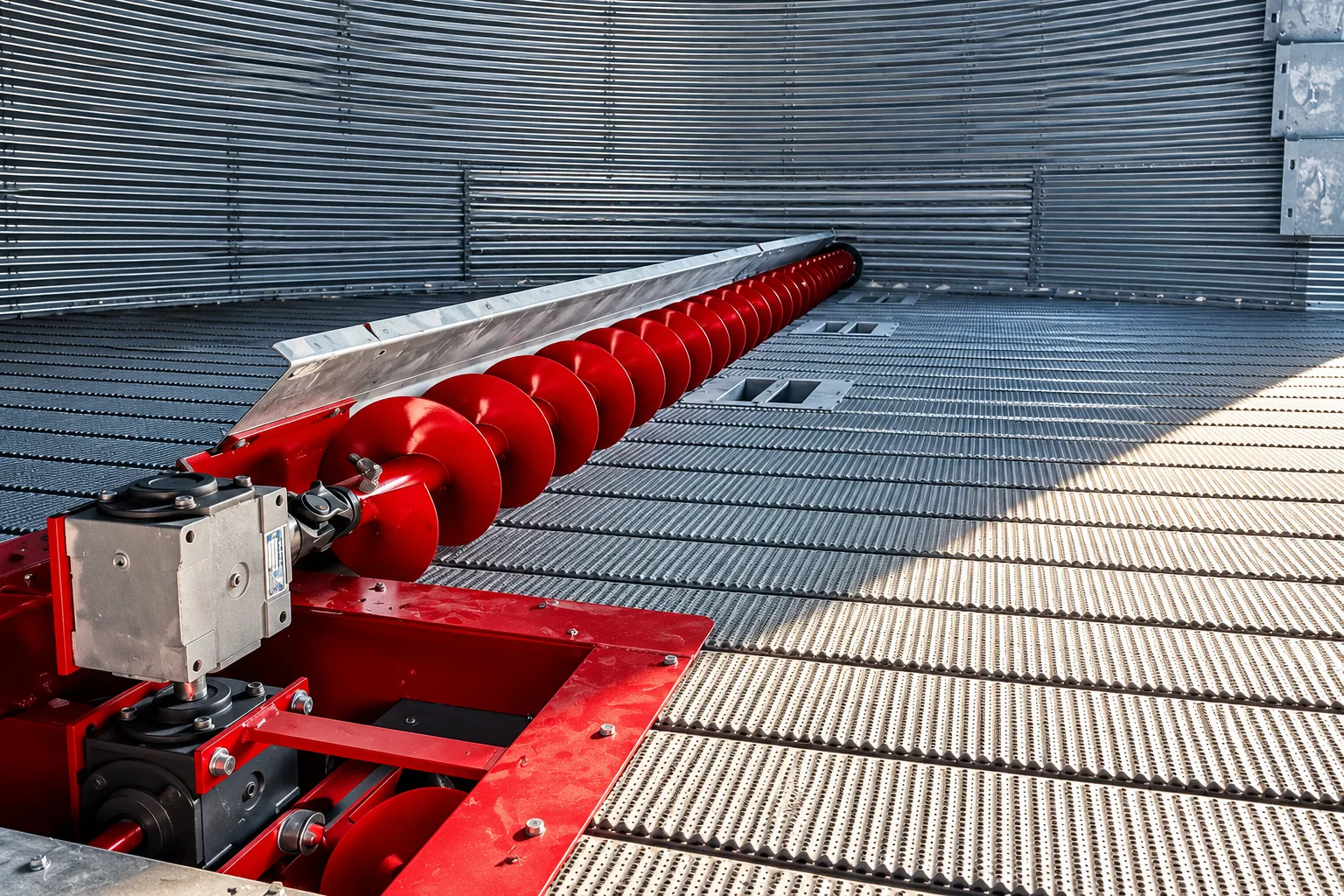 Red grain auger beside corrugated steel grain bins.